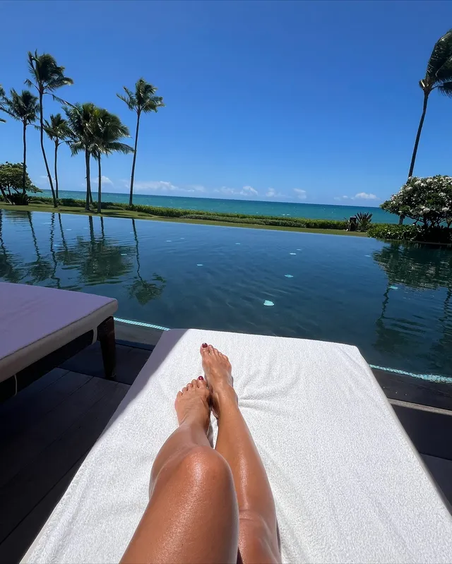 Nicole Scherzinger resting crossed bare legs on a lounger beside a swimming pool.