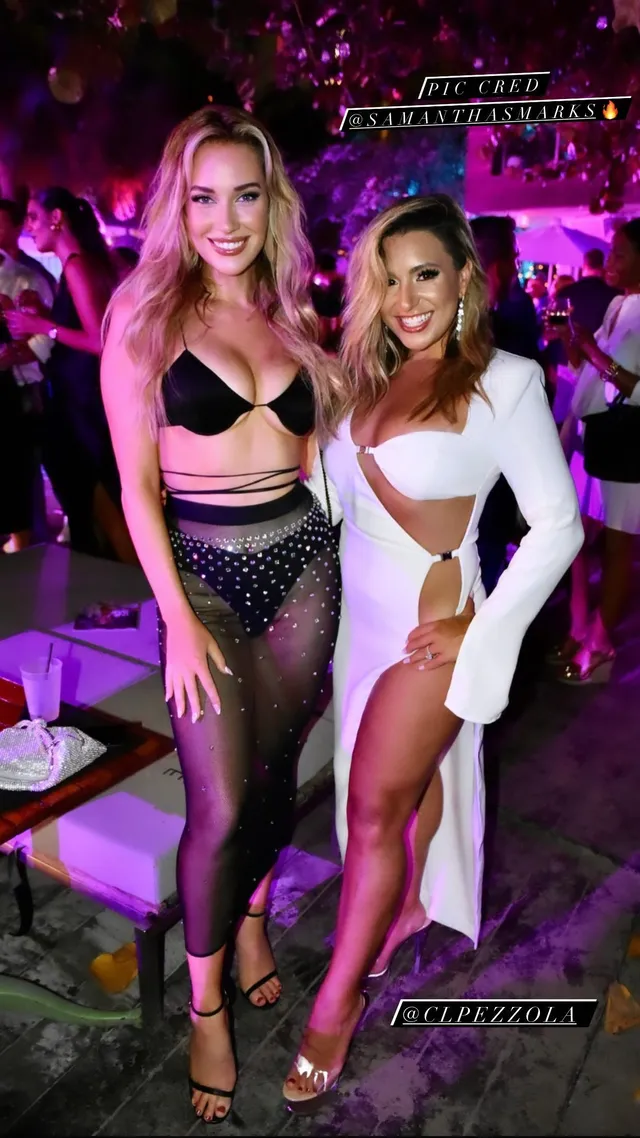 Paige Spiranac posing with a companion at an evening event in black heeled sandals.