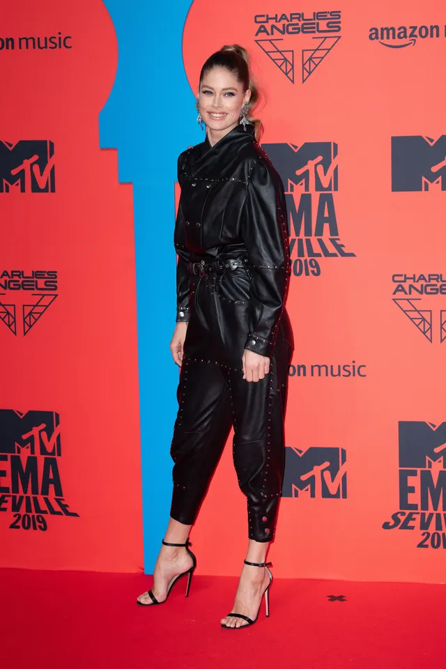 Doutzen Kroes wearing black ankle-strap heels and a black outfit on a red carpet.