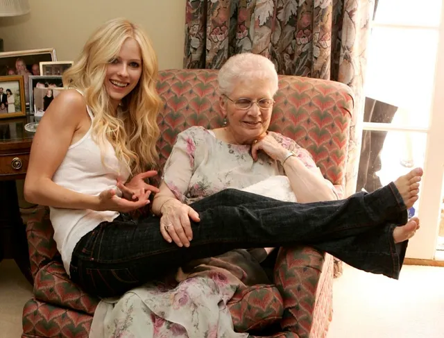Avril Lavigne sitting beside an older person with her bare soles raised.