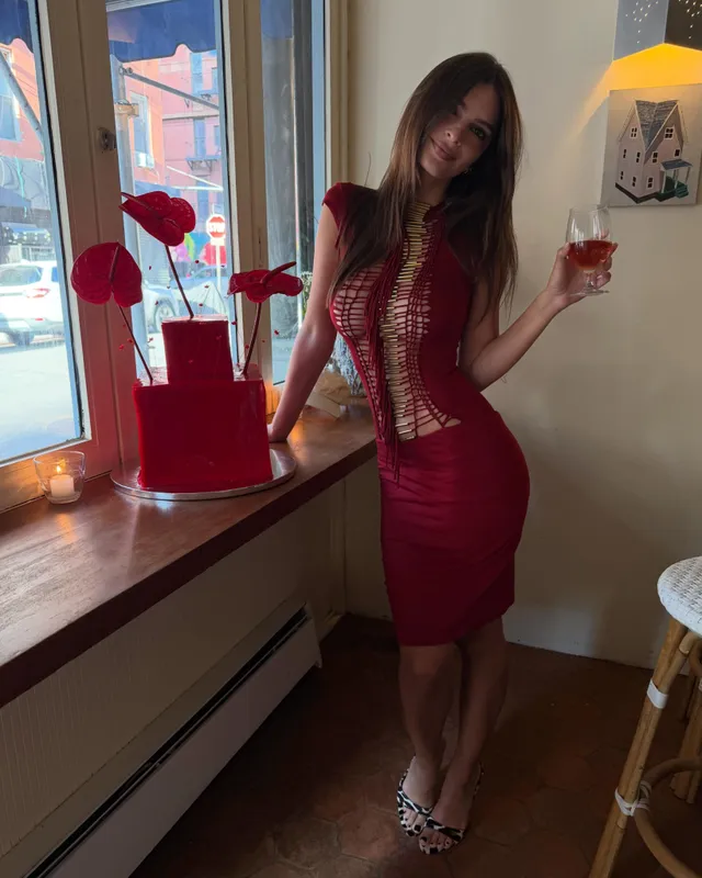 Emily Ratajkowski posing indoors in a red dress and patterned heels.