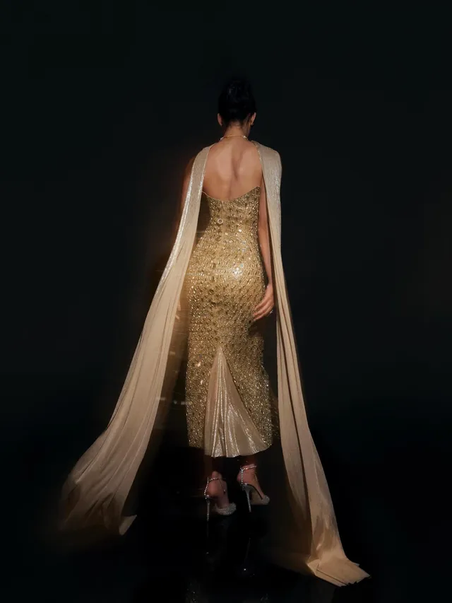 Disha Patani looking back in heeled sandals and a long gold outfit.