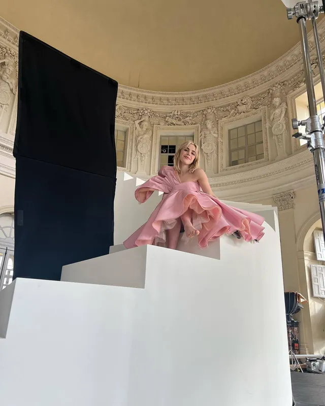 Kiernan Shipka posing barefoot on white steps in a pink dress.