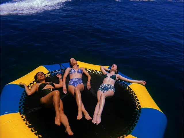 Anna Kendrick relaxing barefoot on a water inflatable with other adults.