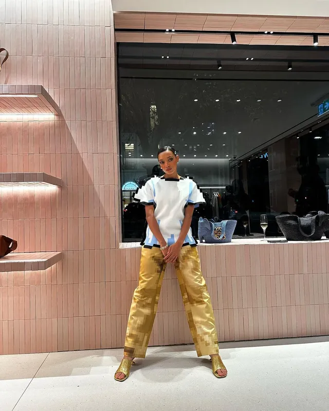 Sophie Wilde posing indoors in gold trousers and heeled sandals.