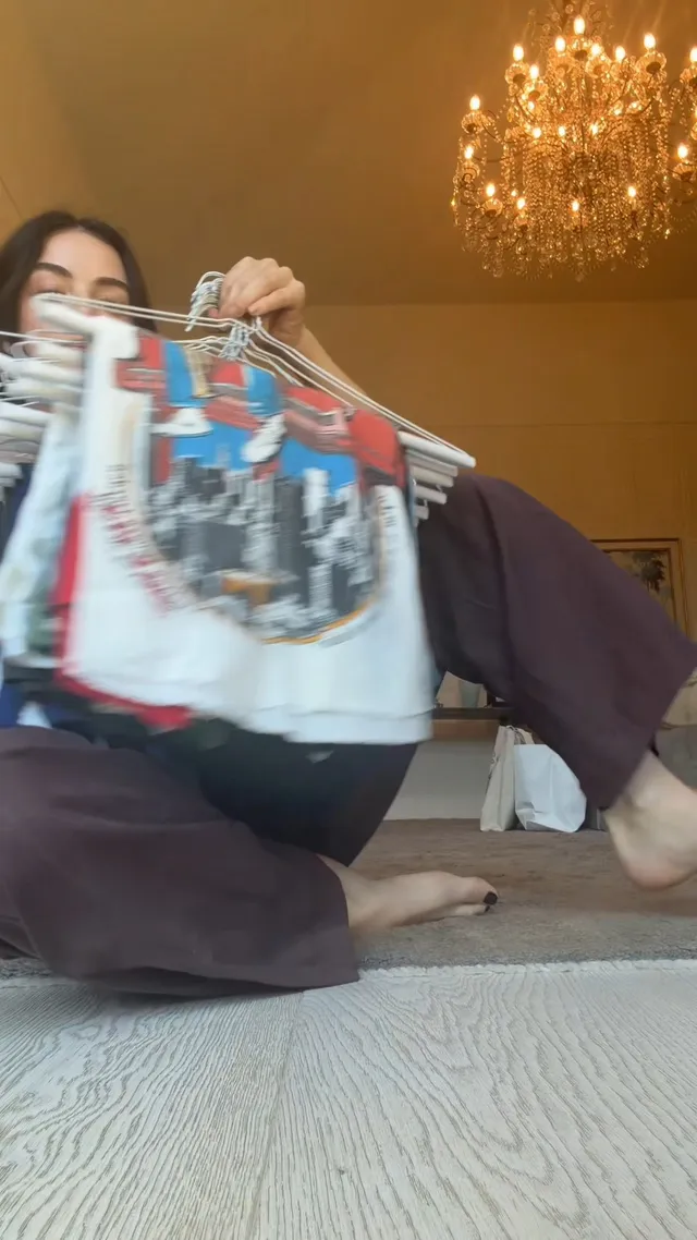 Lucy Hale showing clothes hangers while seated on a rug.