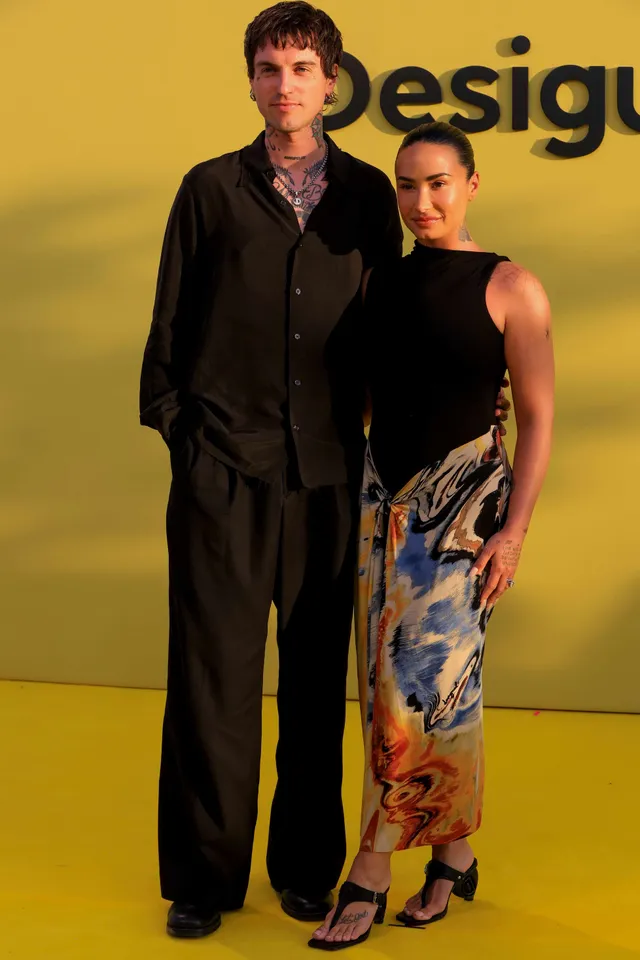 Demi Lovato standing beside another person in patterned trousers and heels.