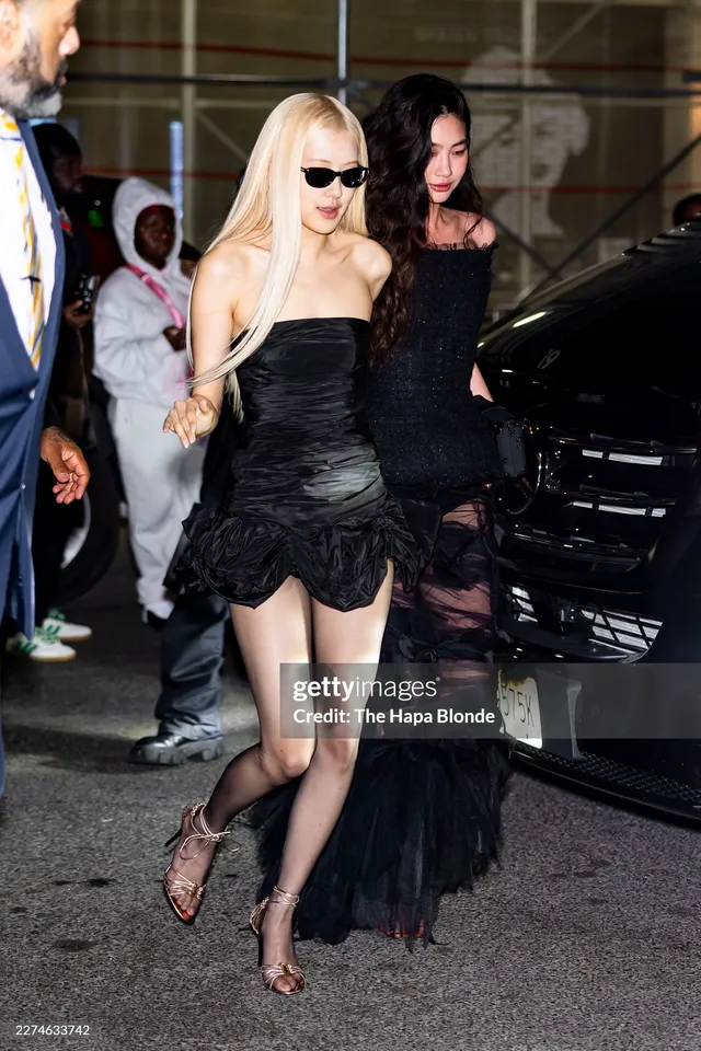 Rosé walking past photographers in sunglasses, a short black dress and high heels.