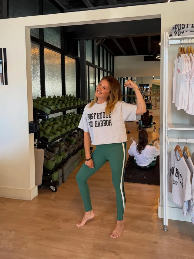 Ashley Tisdale dancing barefoot in a white T-shirt and green leggings indoors.