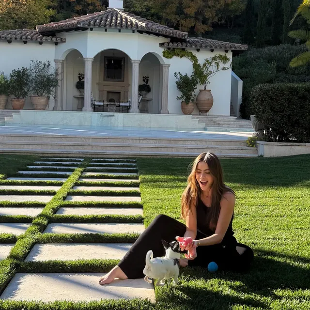 Sofía Vergara sitting barefoot on grass beside a dog.