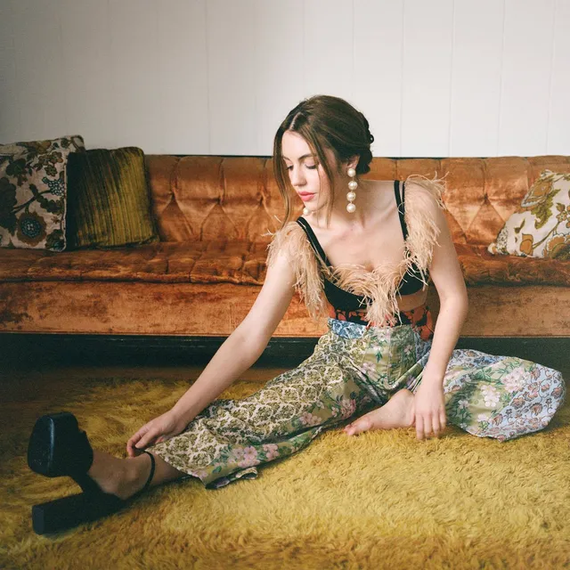 Adelaide Kane sitting on a rug in a patterned outfit.