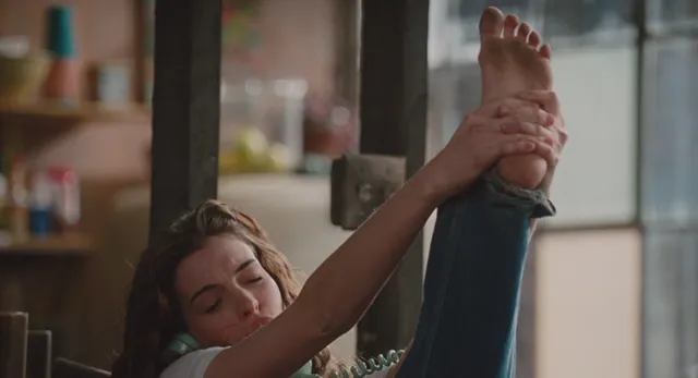 Anne Hathaway holding up a bare foot while stretching.