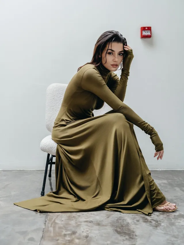 Hande Erçel sitting in an olive gown and clear heels.