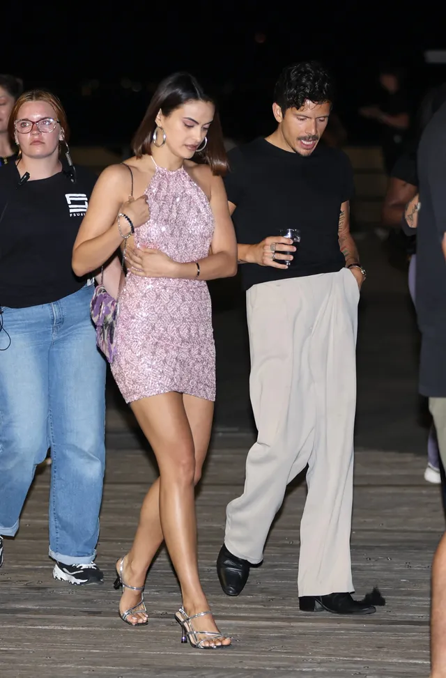 Camila Mendes walking outdoors in a pink dress and clear heels.