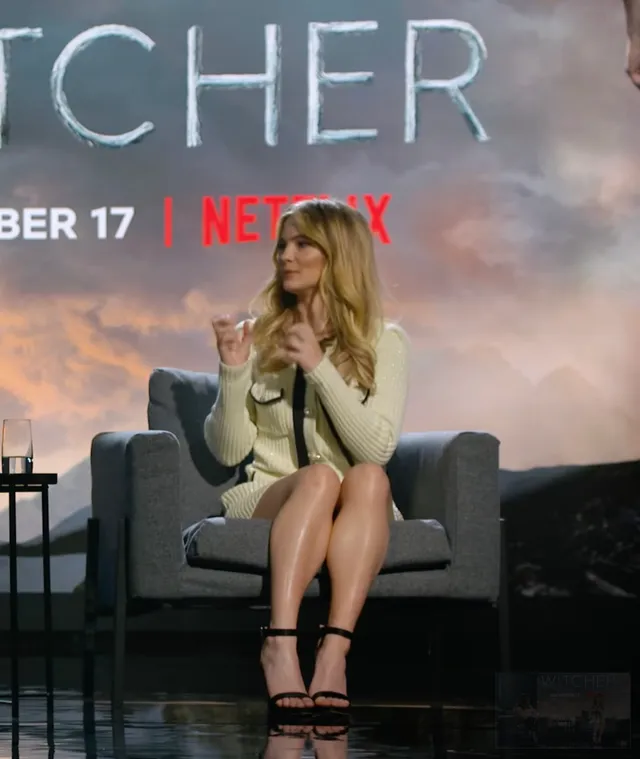 Freya Allan sitting at a panel in a pale outfit and platform heels.