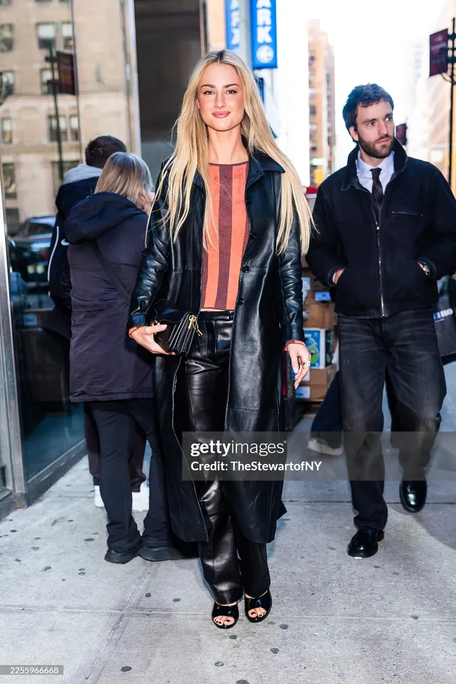 Grace Van Patten walking outside in a black leather coat and open-toe heels.