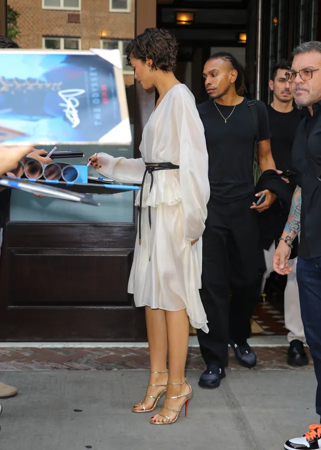 Zendaya walking outside in a white outfit and gold sandals.