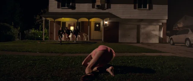 Maika Monroe kneeling barefoot on a lawn at night in a scene.