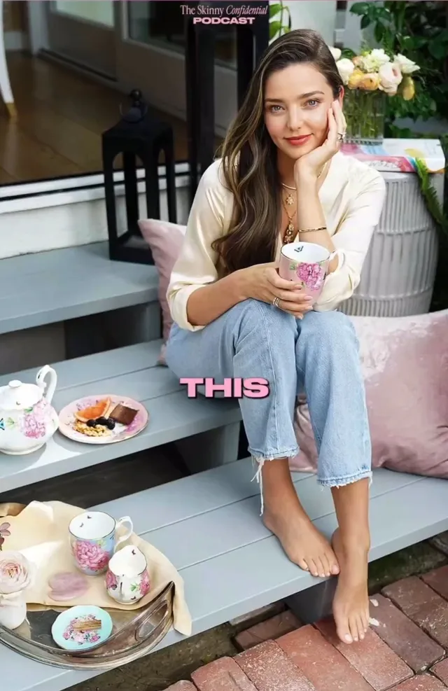 Miranda Kerr sitting barefoot outside beside a table and pink cushions.