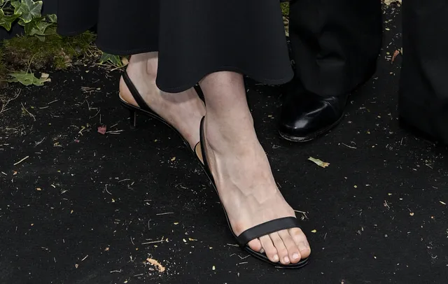 Jodie Comer wearing black sandals beneath wide trousers.
