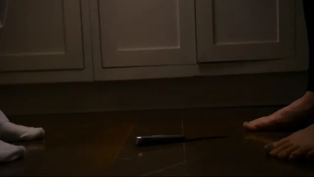 Willa Fitzgerald sitting barefoot on a floor in a scene.