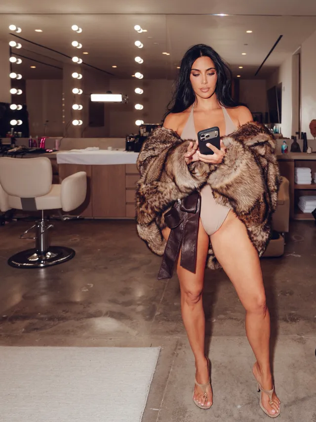 Kim Kardashian posing indoors in a brown coat and heels.