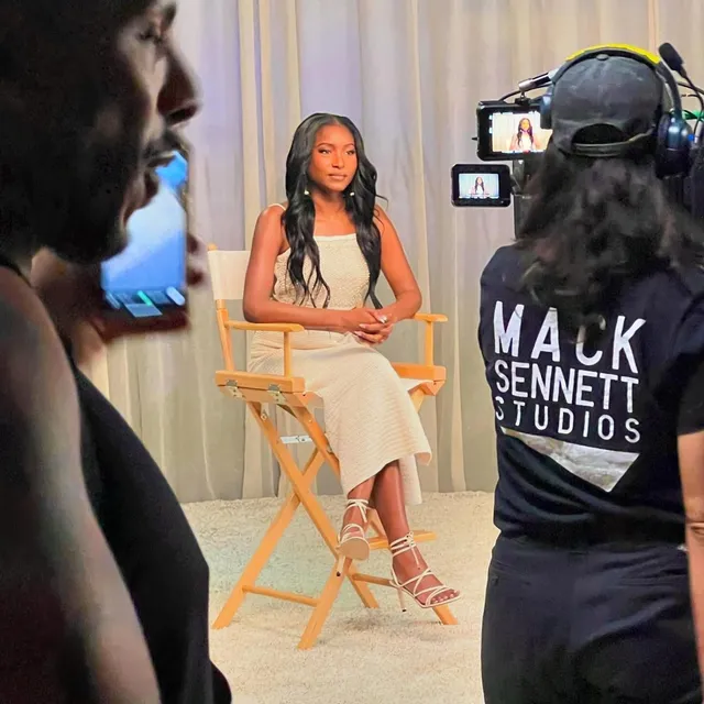 Carlacia Grant sitting for a filmed interview in a pale dress and lace-up heels.