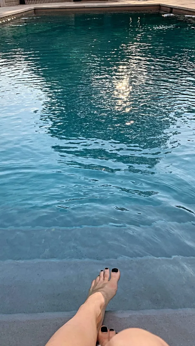 Avril Lavigne resting a bare foot beside a swimming pool.