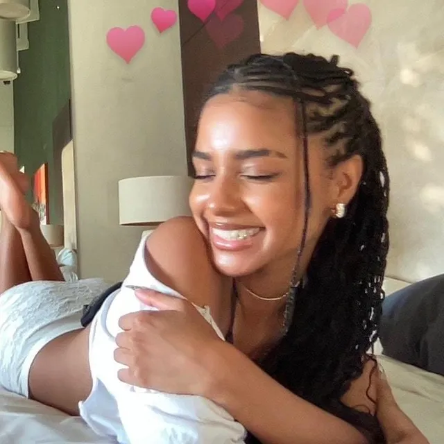 Tyla lying barefoot on a bed during a smiling self-portrait.