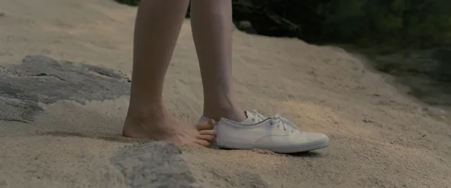 Sophie Thatcher standing with one bare foot beside a white trainer in a film scene.