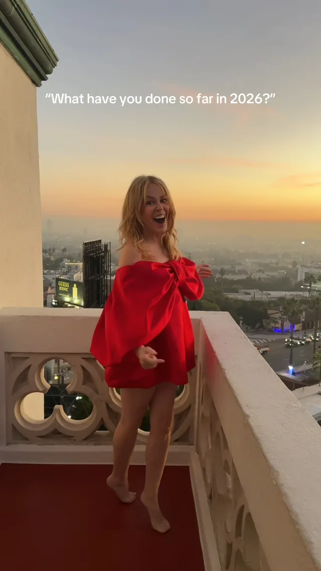 Kylie Minogue a red outfit while standing barefoot on a balcony.