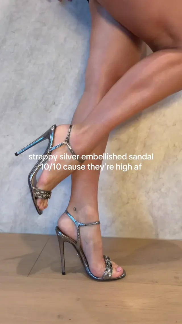 Charli D’Amelio wearing silver embellished high heel sandals indoors.