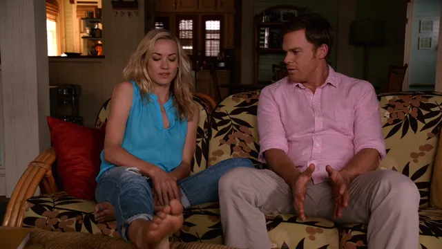 Yvonne Strahovski sitting beside a companion on a sofa during a screen scene.