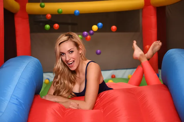 Paige Spiranac reclining on an inflatable play structure with her bare feet raised.