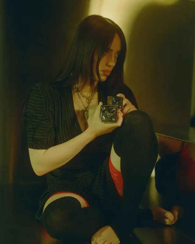Billie Eilish a casual black outfit in a dim room.