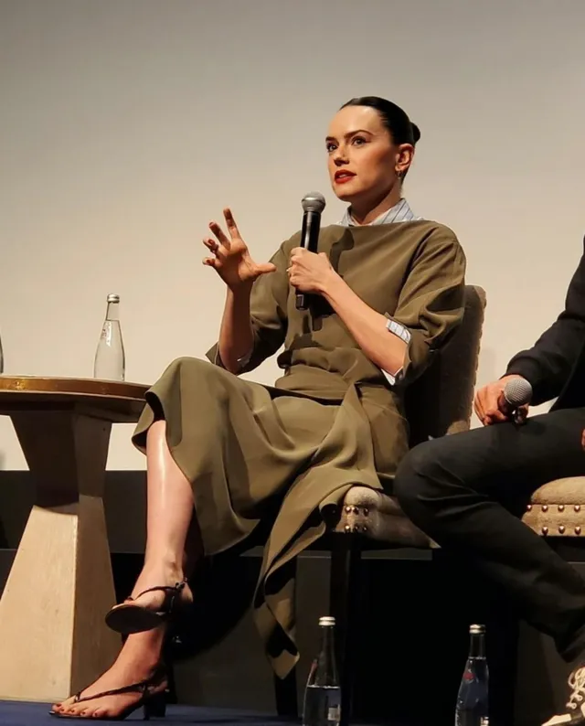 Daisy Ridley speaking into a microphone while seated onstage.