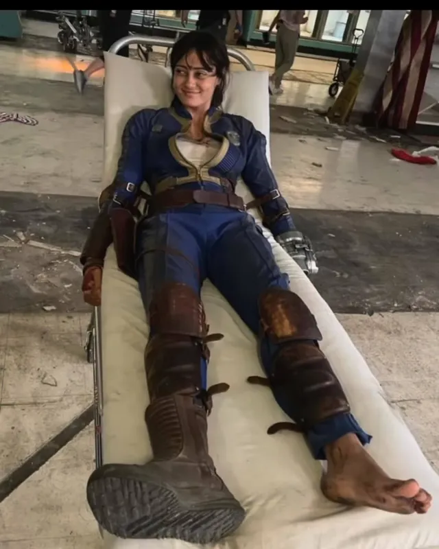 Ella Purnell sitting in a costume chair on a film set.