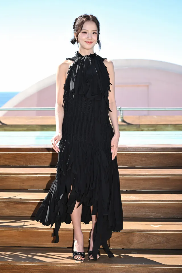 Jisoo wearing black heeled sandals beneath a long black dress outdoors.
