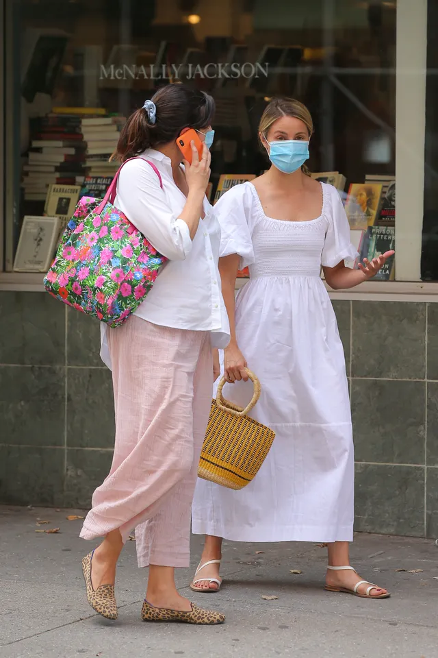 Dianna Agron walking beside a companion in a white dress and flat sandals.