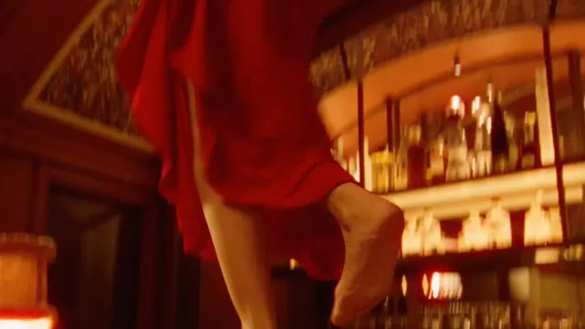 Ester Expósito wearing turquoise pointed heels beneath a red outfit during a screen scene.