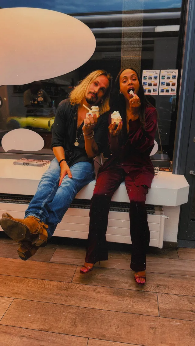 Zoe Saldaña sitting beside a companion in heeled boots.