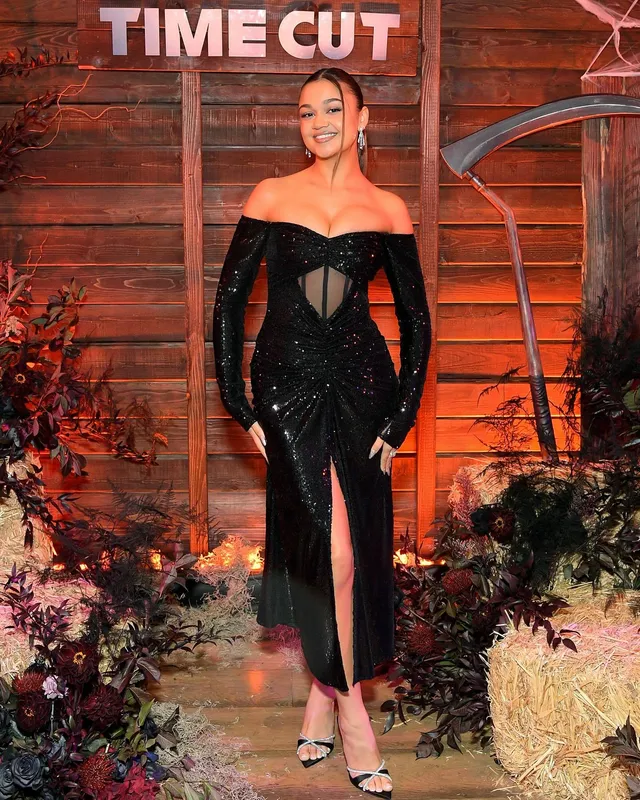 Madison Bailey posing in an off-shoulder black dress and patterned heels at a premiere.