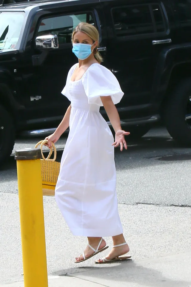 Dianna Agron walking outdoors in a white dress and flat sandals.