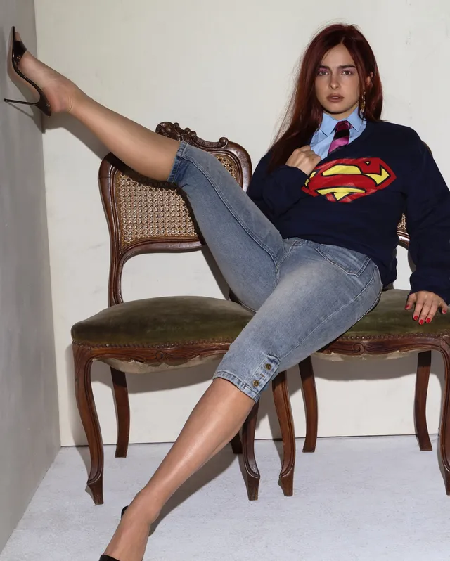 Addison Rae seated in a chair wearing jeans and pointed black heels.