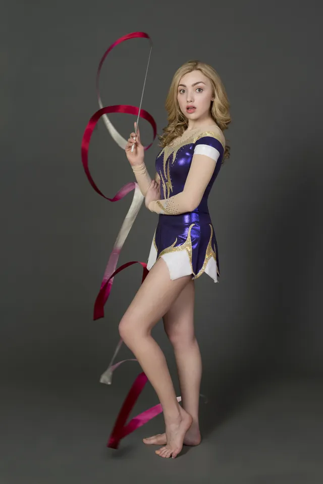 Peyton List posing barefoot with a ribbon in a studio.