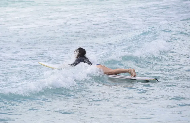 Suki Waterhouse paddling a surfboard on the sea.