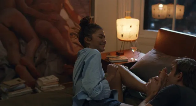 Zendaya: seated barefoot on a bed during a film scene.