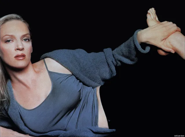 Uma Thurman reclining barefoot in a gray outfit.