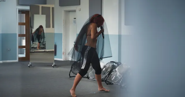 Naomi Scott standing barefoot in dark cropped rehearsal trousers.