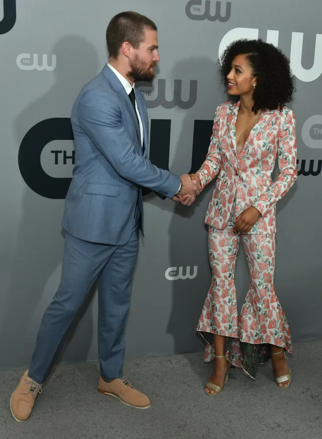 Samantha Logan posing beside a man in a floral trouser suit and heels.